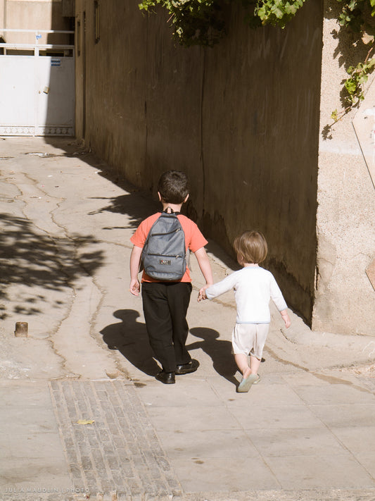 Two schoolboys with backpacks walking home hand in hand in Shiraz, Iran